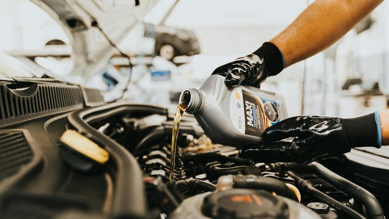 Technicien en vitrage auto répare un pare-brise fissuré dans un garage, en uniforme gris, masque et gants noirs.