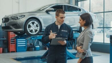 Un mécanicien français montre un document à une cliente dans un garage moderne, voiture sur pont.