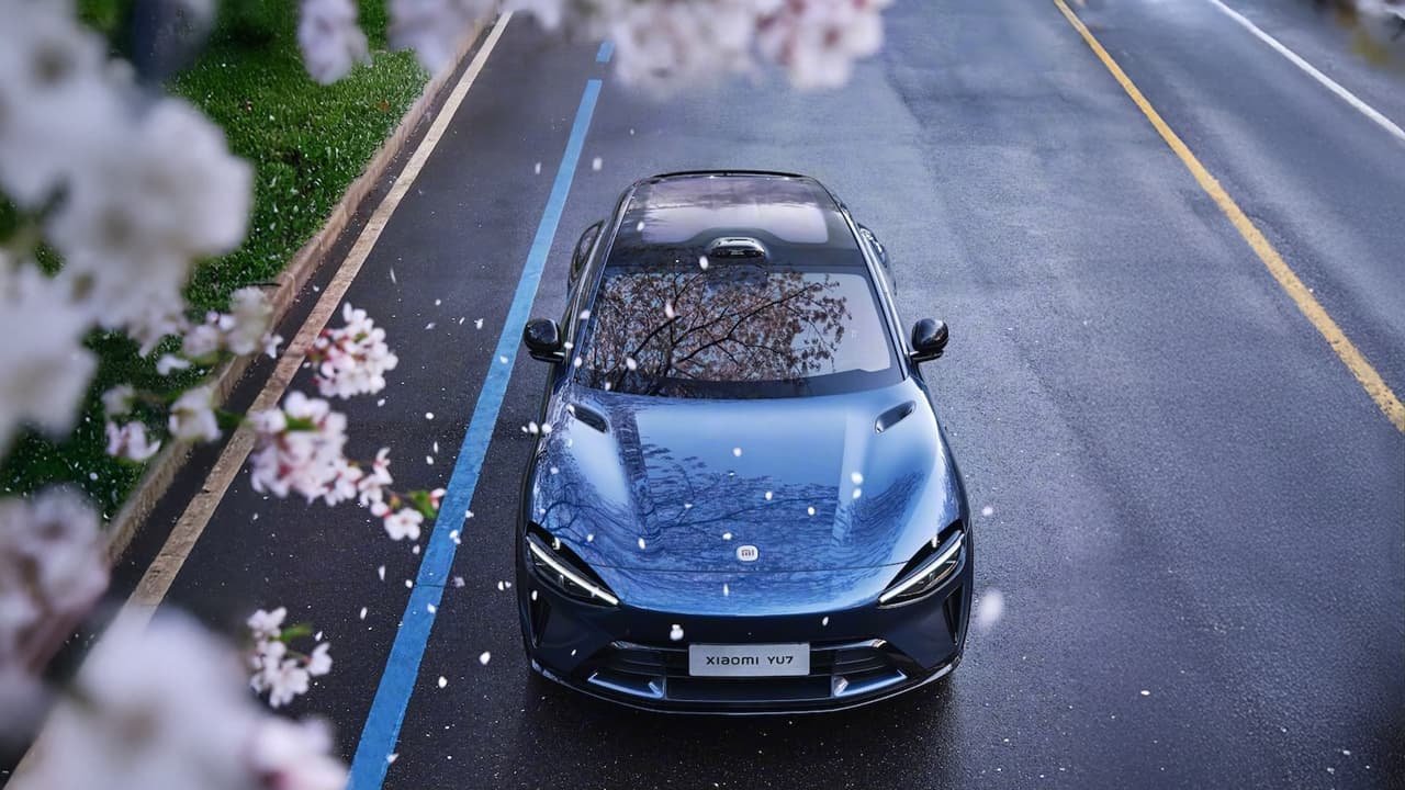 La Xiaomi YU7 bleue, élégante, est garée sous des fleurs tombantes, route mouillée, ambiance printanière